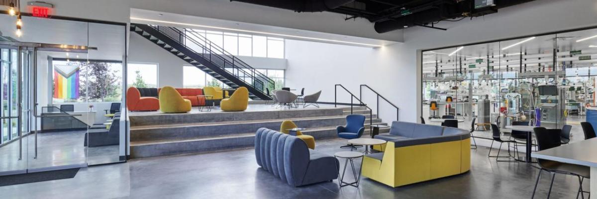 A lobby with blue and yellow seats, which also has a large window looking into a lab