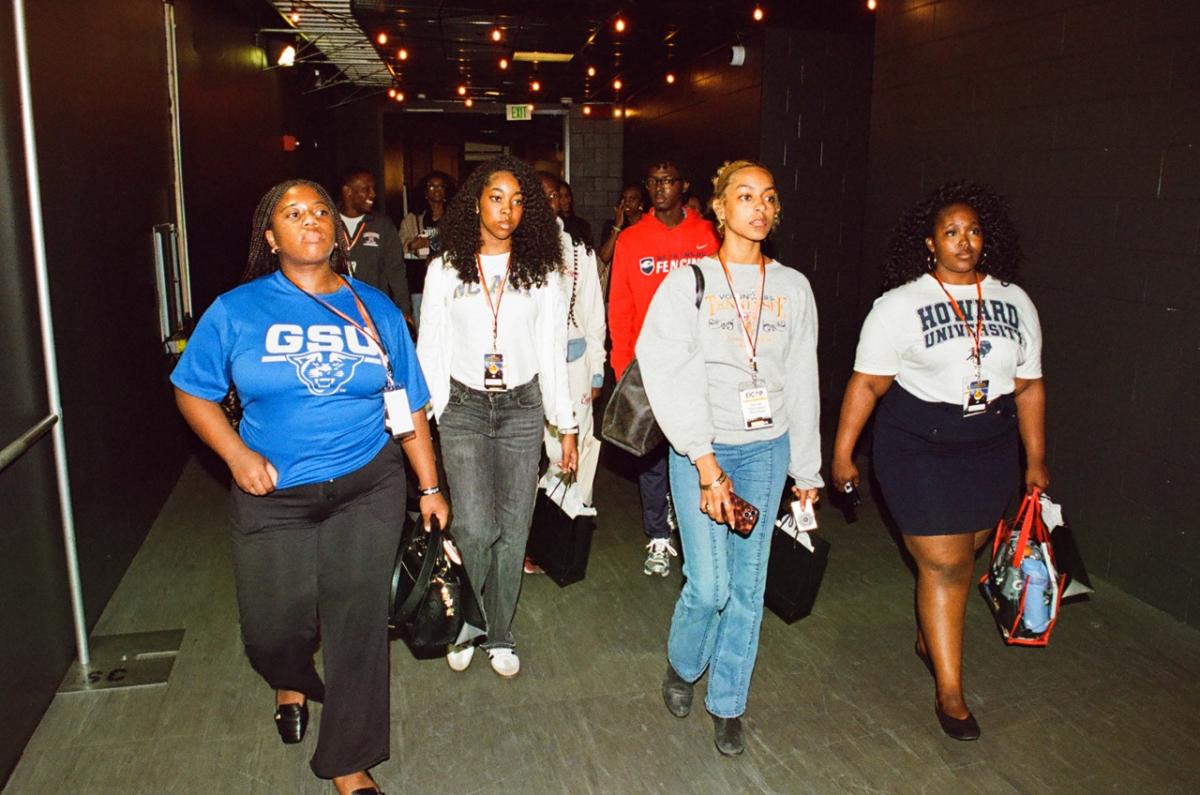 Group of event participants walking together through a Crypto.com Arena corridor, wearing name badges and carrying bags.