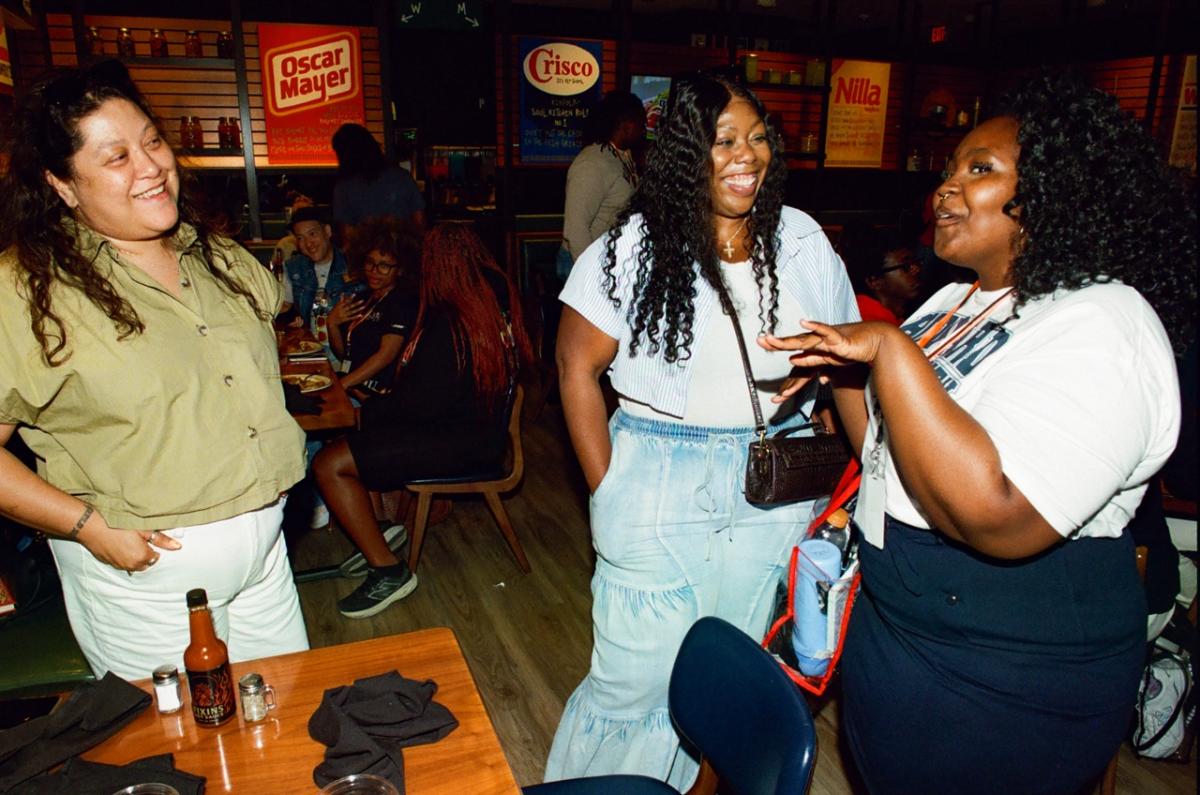 Attendees socializing and networking around tables in a restaurant-style setting with branded signage visible in the background.