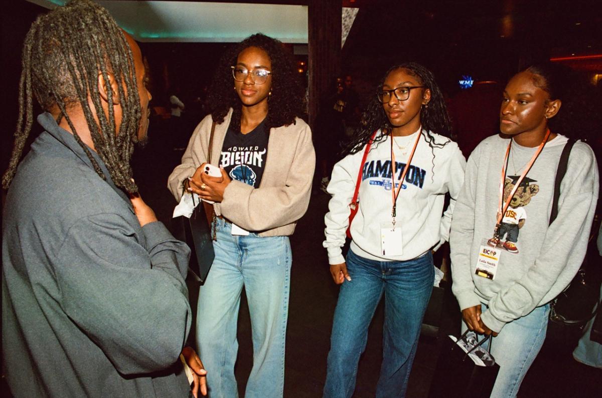 Small group of attendees wearing lanyards engaged in conversation inside an event space at Peacock Theater.