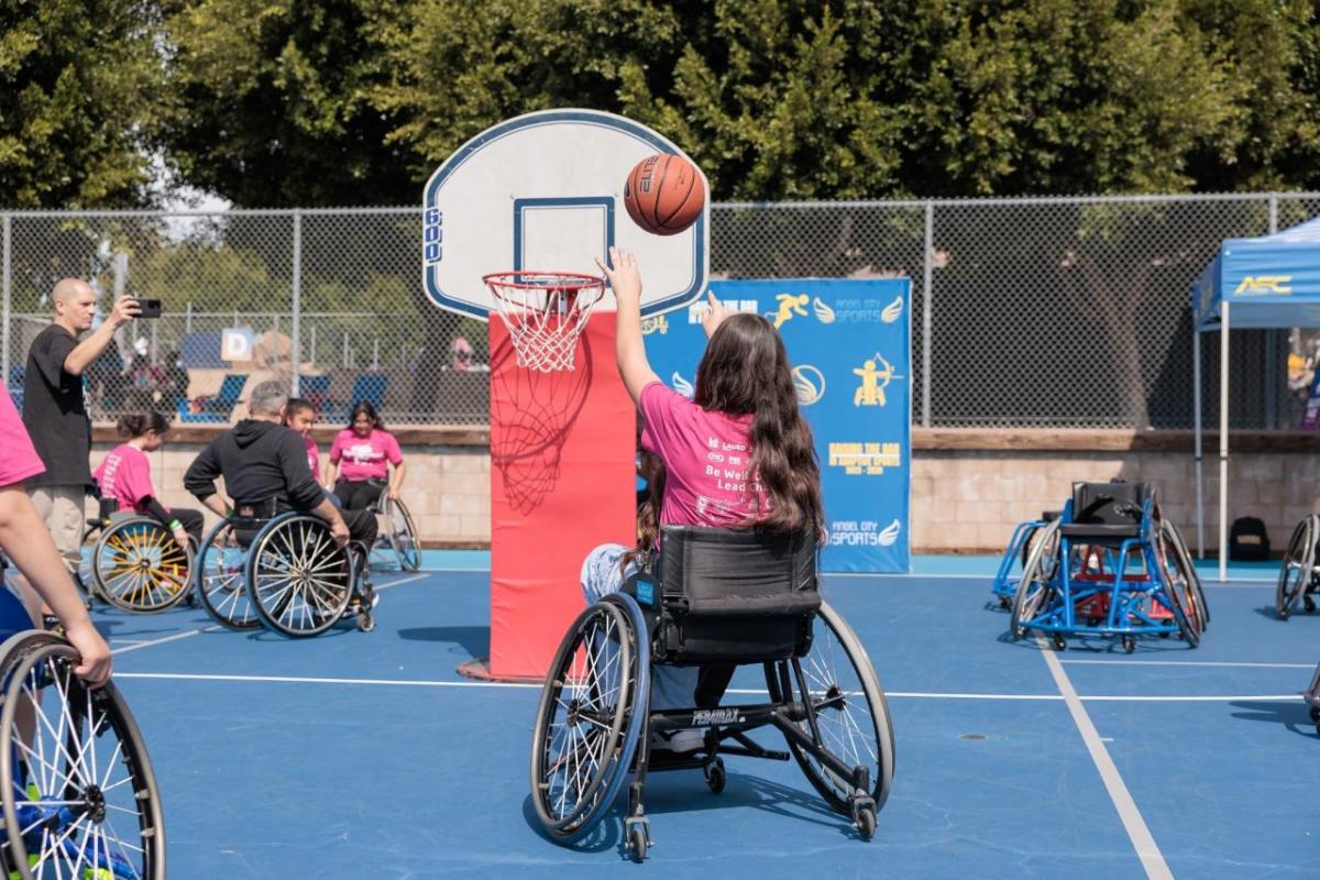 A girl in a sports wheelchair shoots a basketball during an adaptive sports activity at Girls Empowerment Day.