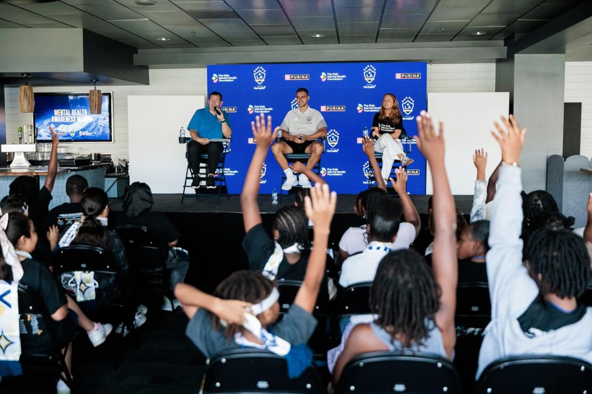 Panel discussion on stage at an LA Galaxy event as youth attendees raise their hands to ask questions.