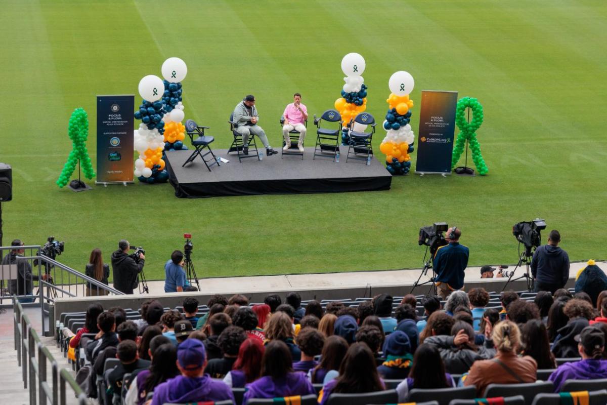 An outdoor audience watches people seated on a stage