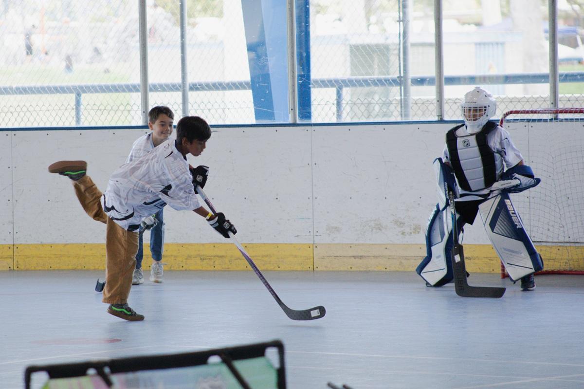 A youth participant takes a shot on goal during a ball hockey game while a goalie prepares to make a save on an indoor sports court.