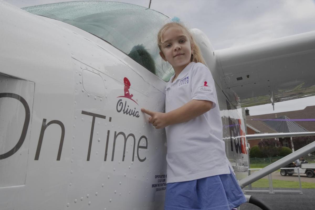 Young girl standing next to plane, pointing at her name (Olivia) printed on it.