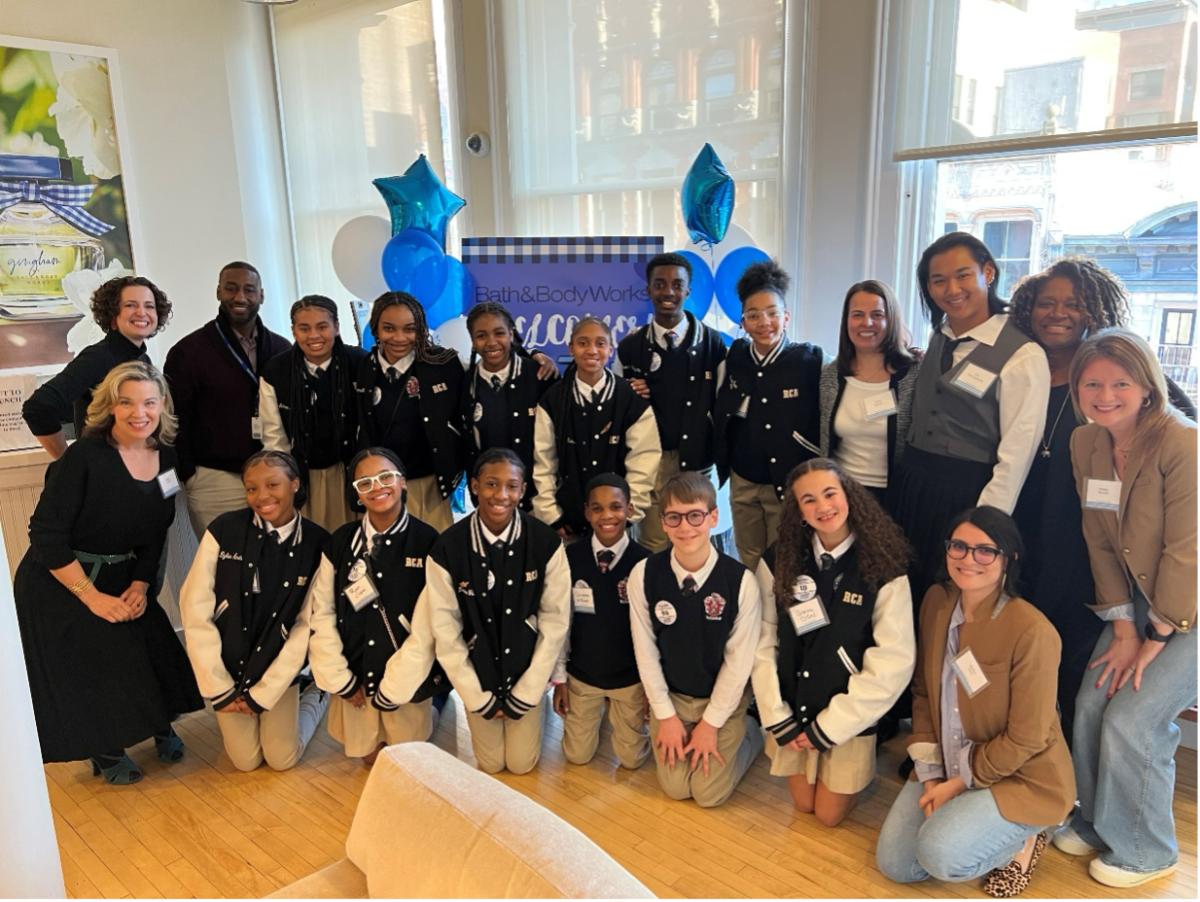 12 middle school students smile alongside seven Bath & Body Works employees in front of a sign with balloons and sunny windows.