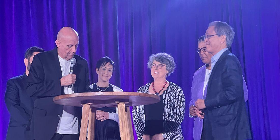 People collected together on a stage around a wooden table