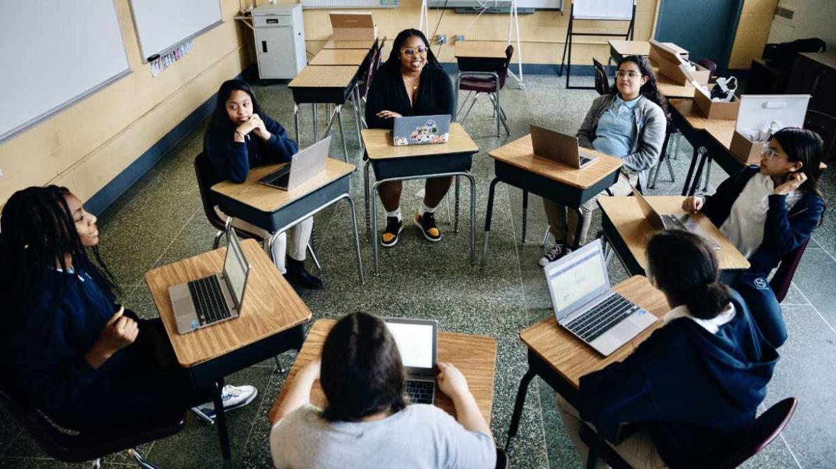 A group of people sat at desks in a circle using laptops