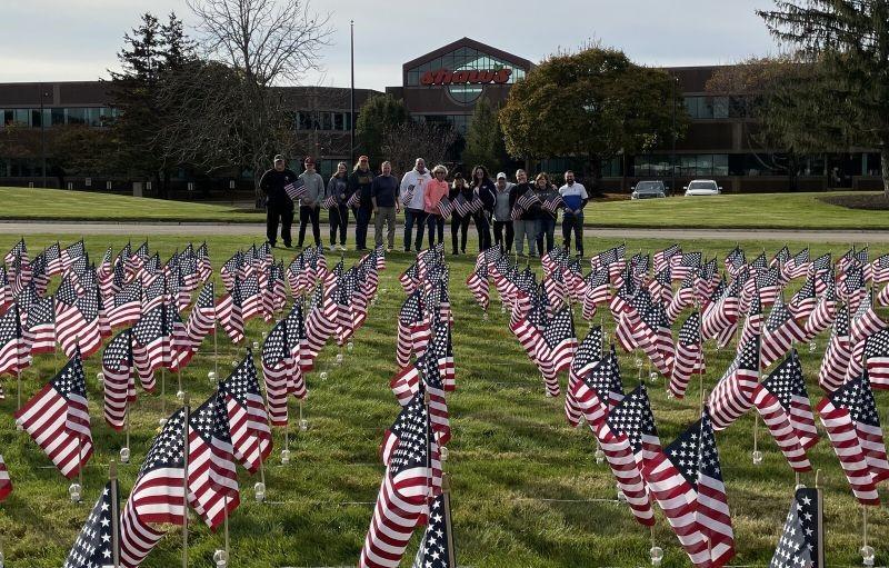 Group of people posing behind field with flags in front of Albertsons Cos' Shaw's Store Support Center Sign