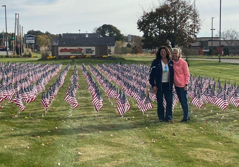 Two people posing in front of field with flags in front of Albertsons Cos' Shaw's Store Support Center Sign