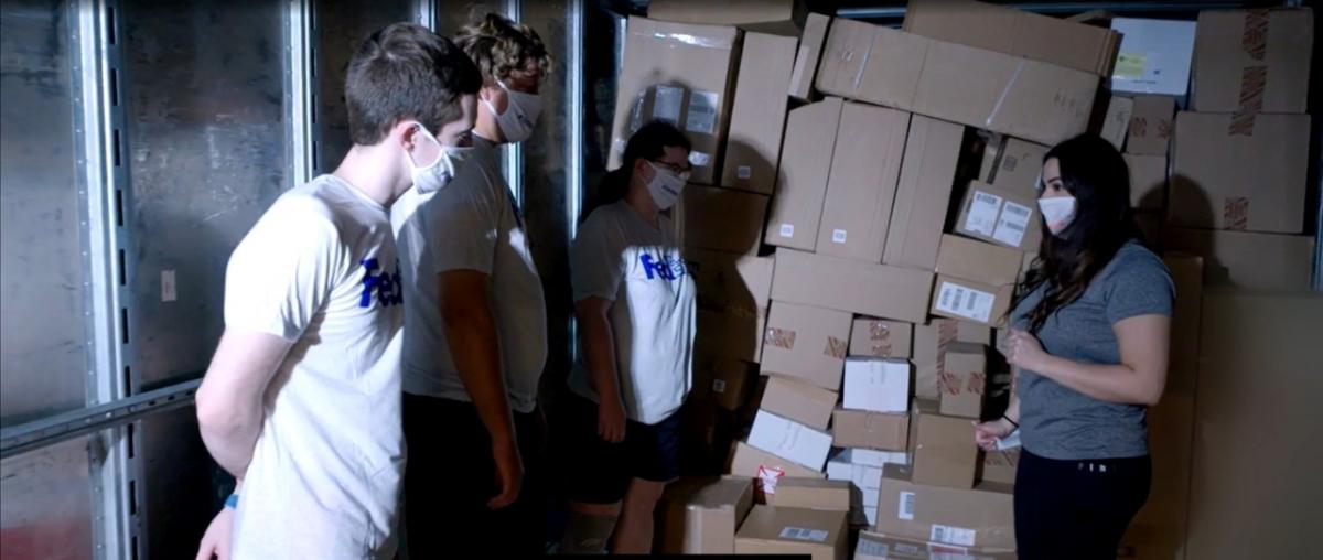 Image of 4 people standing in front of a stack of shipping packages