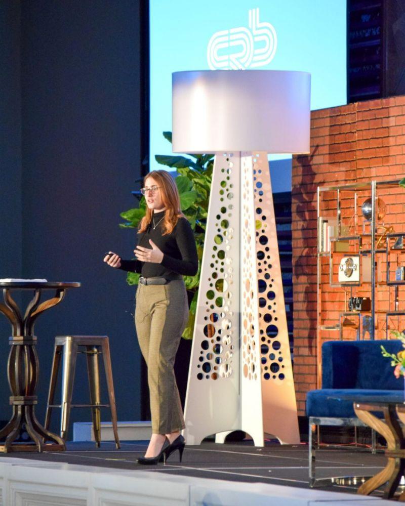 Sara Lanning standing on stage with various furniture and plants around her