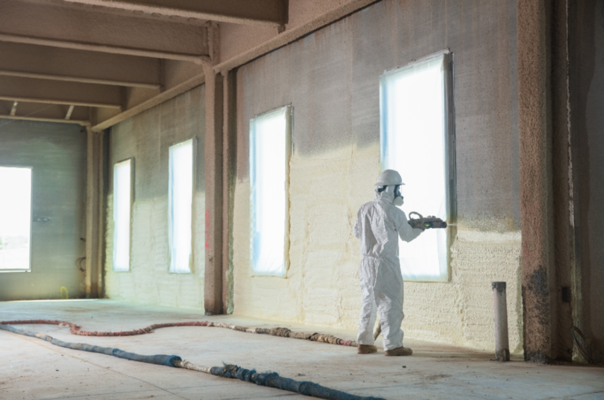 worker in safety gear sprays insulation onto a wall