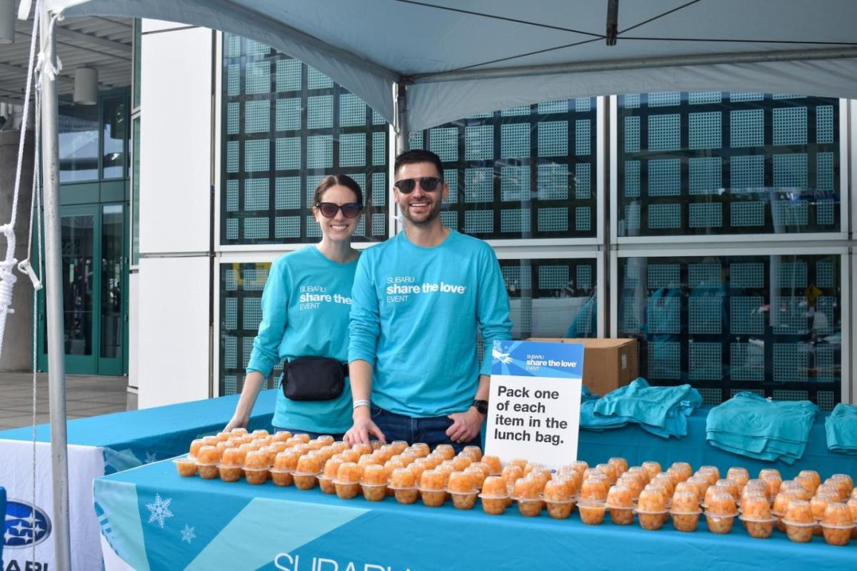 Two people standing behind a table with food items on it