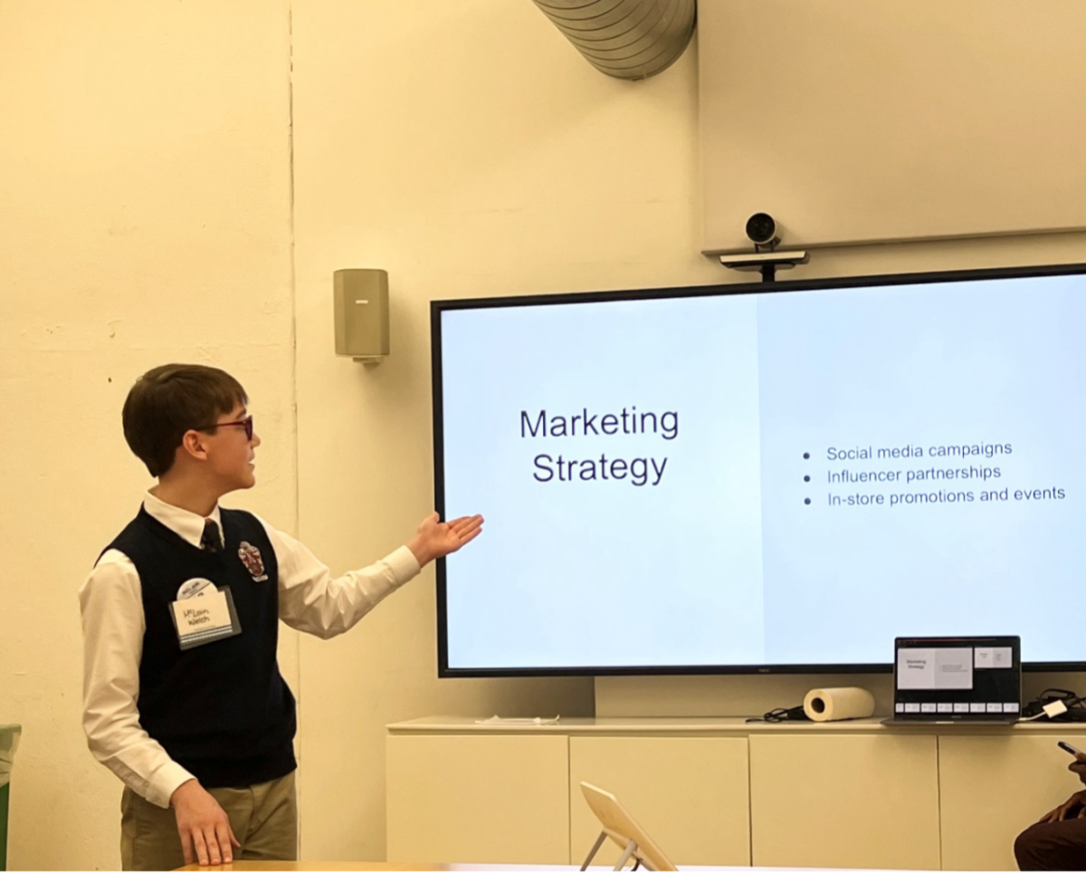 A male middle school student stands in front of a screen and points to information on a Power Point slide.
