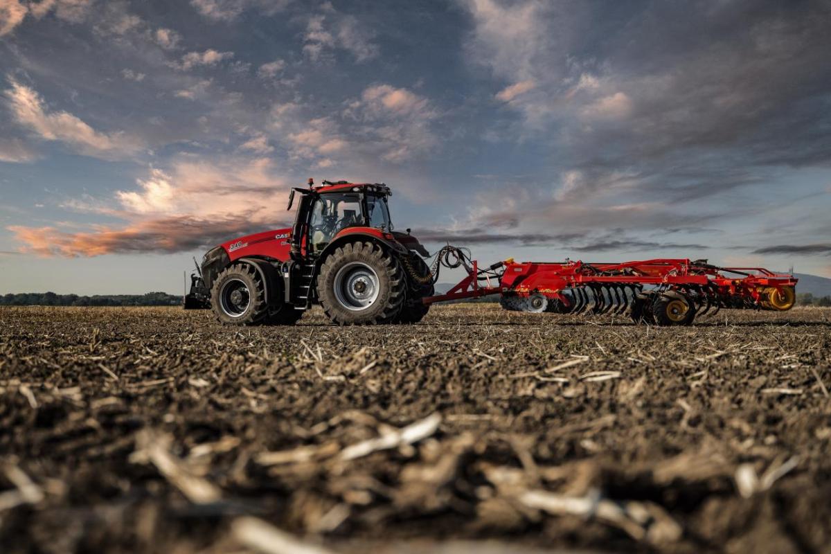 A red tractor in a field with cloudy sky behind it