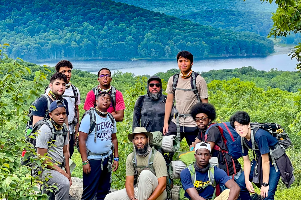 A group in hiking gear, posing for the camera with a tree-covered hill and a lake behind them