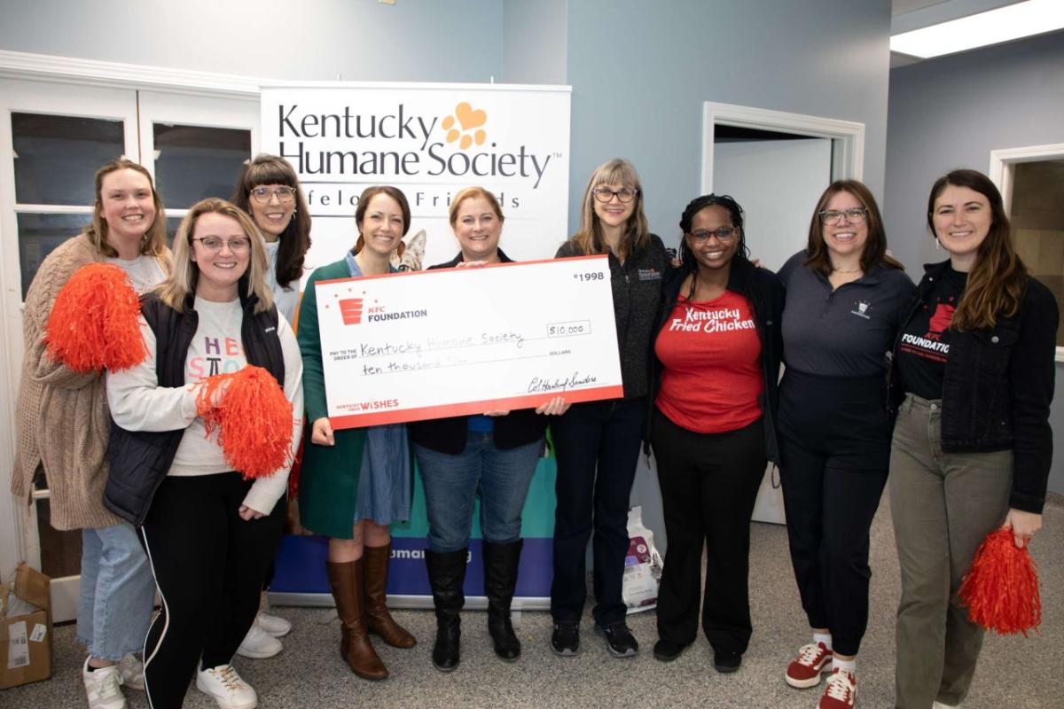 People standing together inside, two of them holding a large check