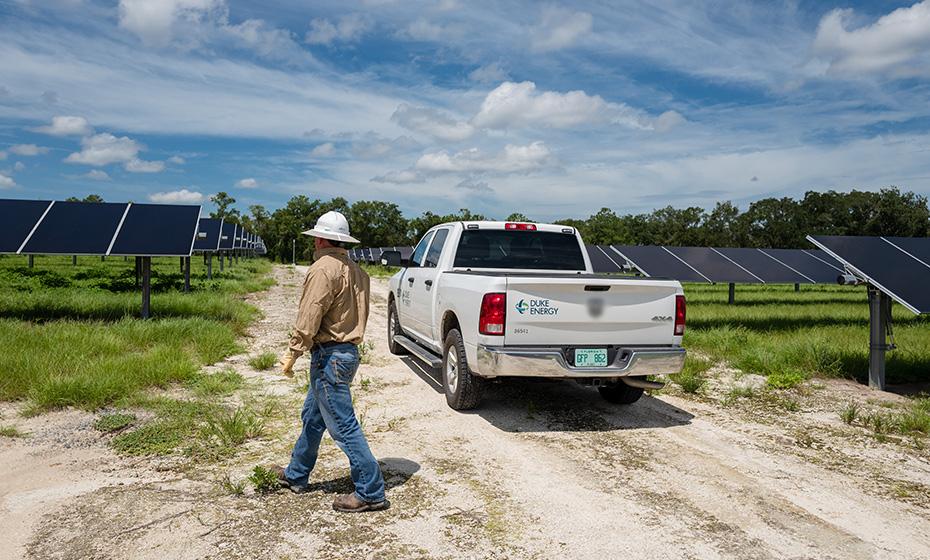 Duke Energy employee in a hardhat inspecting solar panels in a grassy field