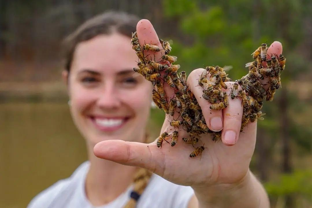 Leigh-Kathryn Bonner signing "I love you" with a hand covered in honeybees