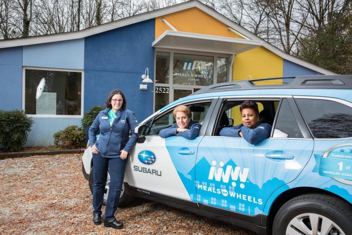 People in and around a stationary Meals on Wheels car