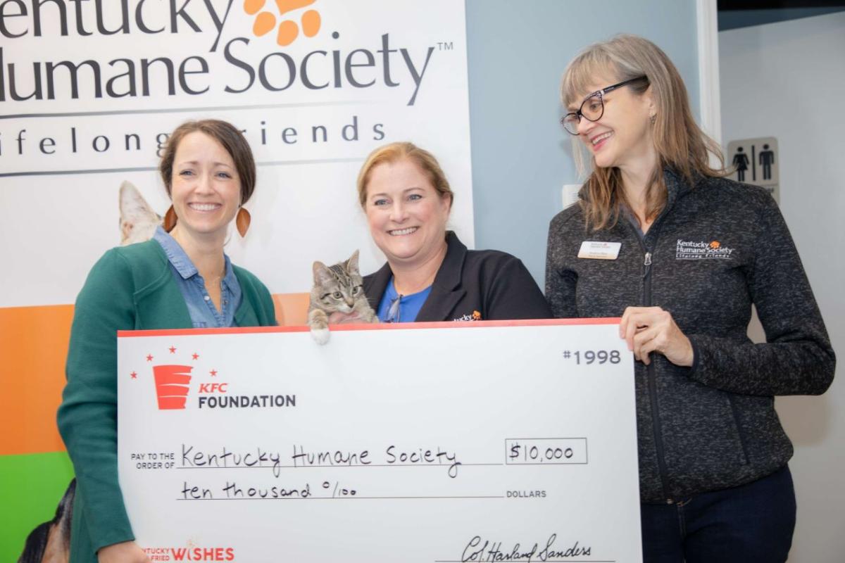 Three people holding an oversized check, with a cat peeking over the top