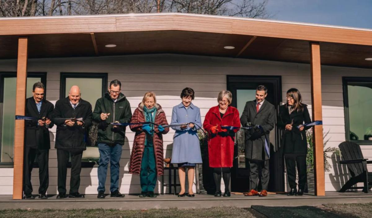 A group of people standing on the porch of the 3D printed home each cutting a portion of the ribbon.