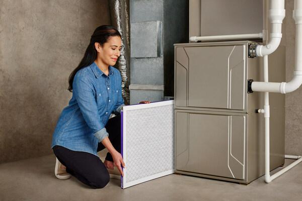 Woman installing a 3M air filter into an HVAC unit.