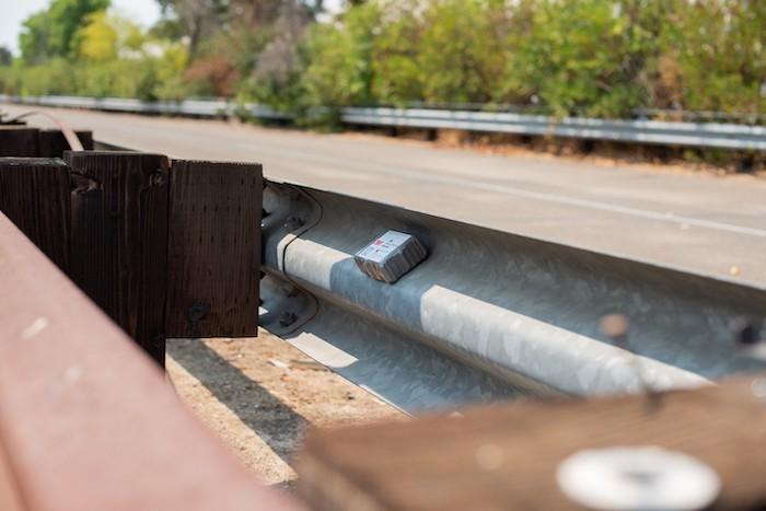Close up of a guardrail with a 3M monitoring device for highway safety.
