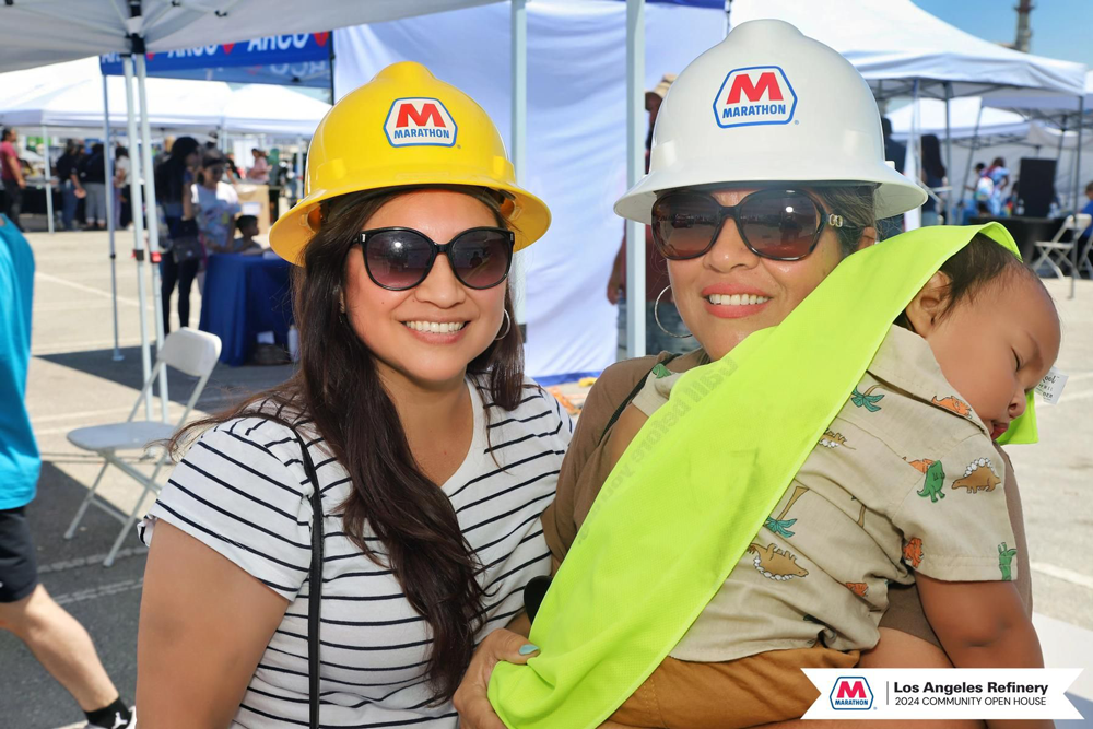 Two people in hard hats smiling - one holding a baby