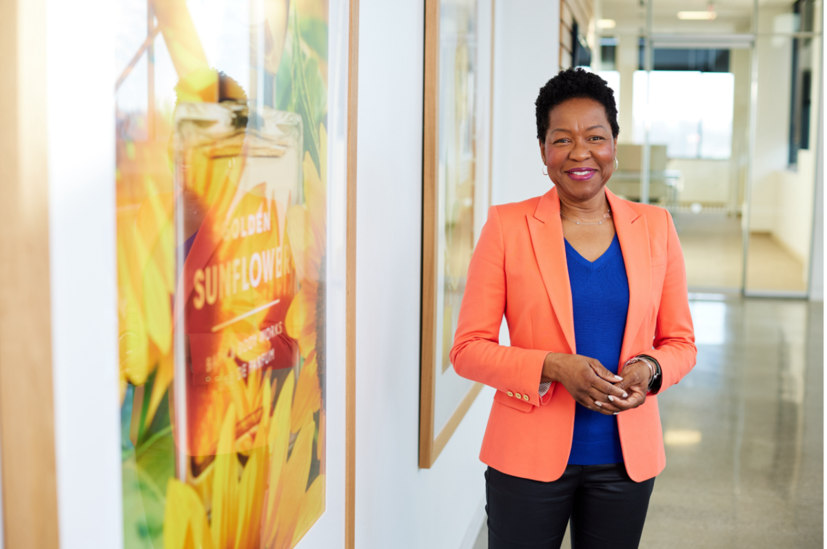 A person in an orange jacket standing in a hallway next to large photographs of Bath & Body Works products