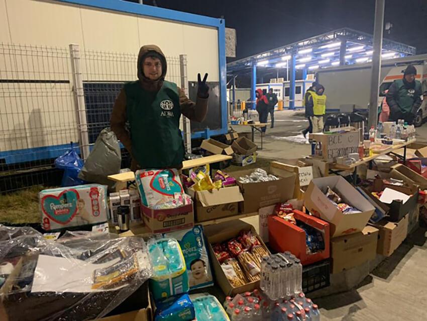 aide worker standing behind a row of boxes of supplies like diapers, water, soaps.