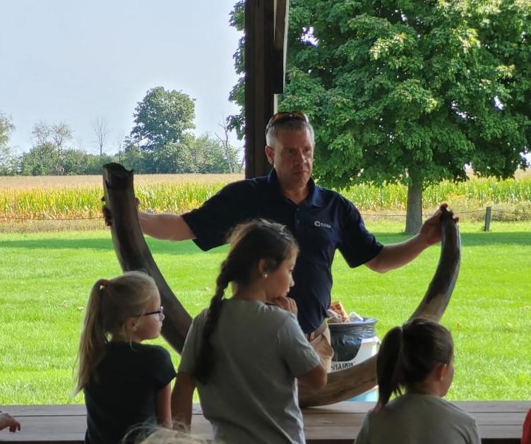 An adult holding a large tusk on a picnic bench as kids watch on.