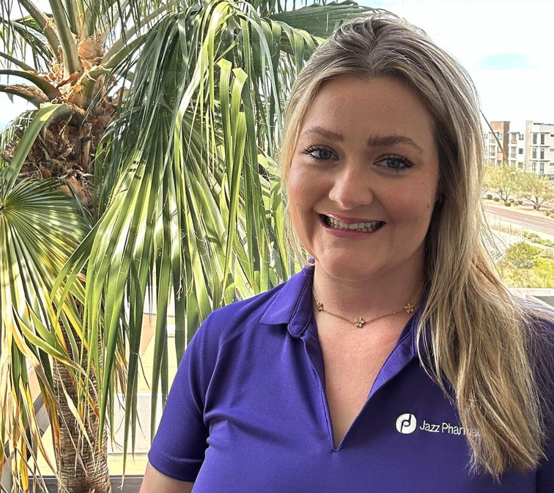 Smiling person wearing purple with a palm tree behind them