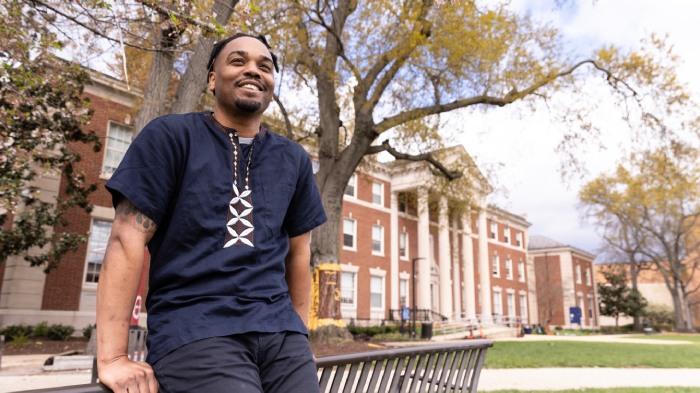 Dr. LeNiles leaning on a bench in front of a tree