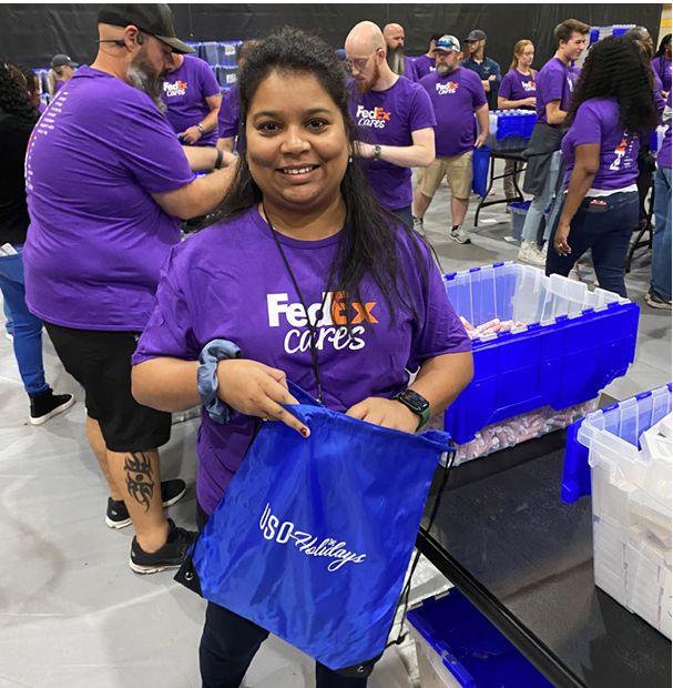 Volunteers in groups packing blue bags. One smiling at the camera.