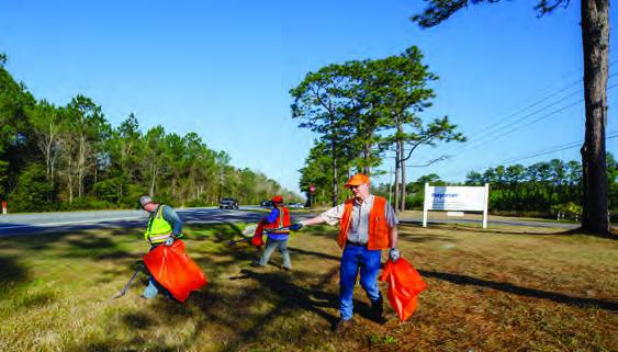 Three people working together outside to clean a grassy area