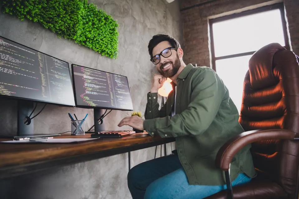 Portrait of professional hacker young man sitting chair computer desk loft interior office indoors. GETTY " "