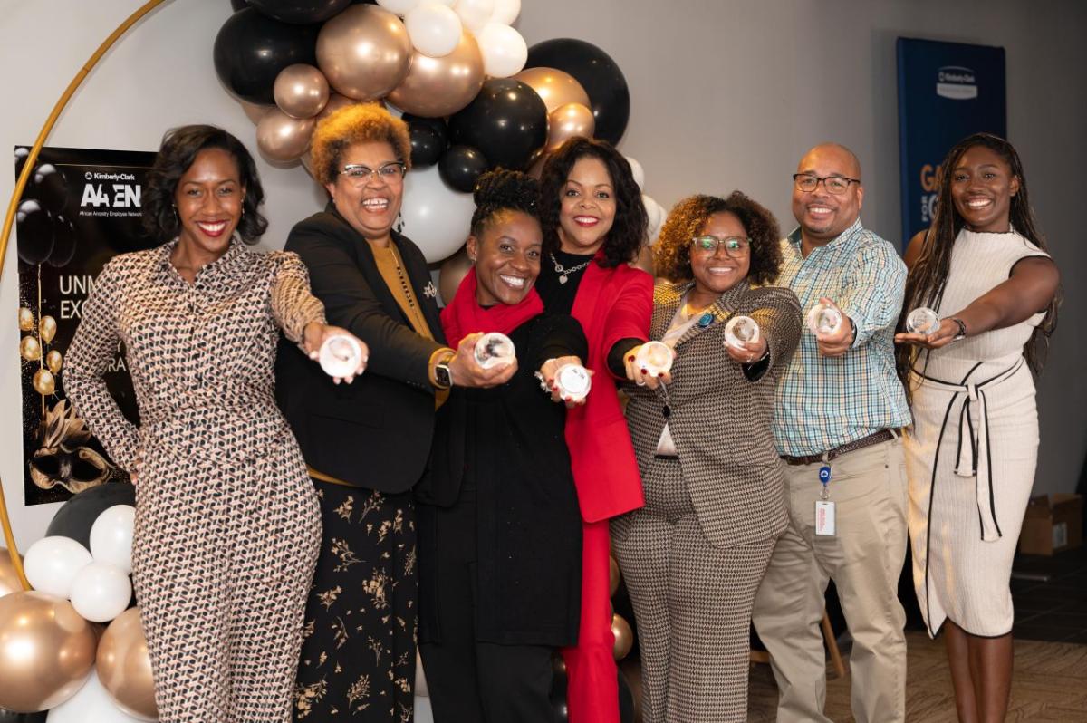 A line of smiling people posed, each holding out a round object.