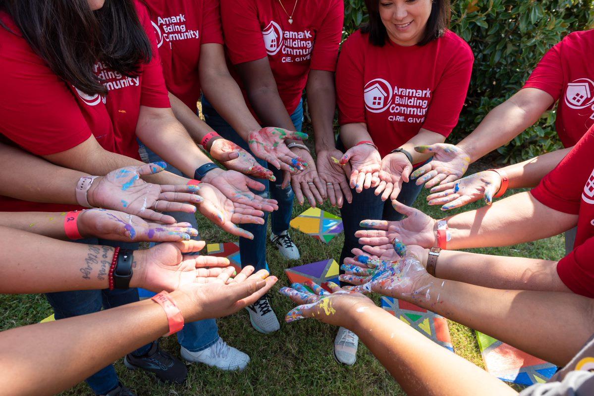 Aramark volunteers display their paint-covered hands in a circle outside