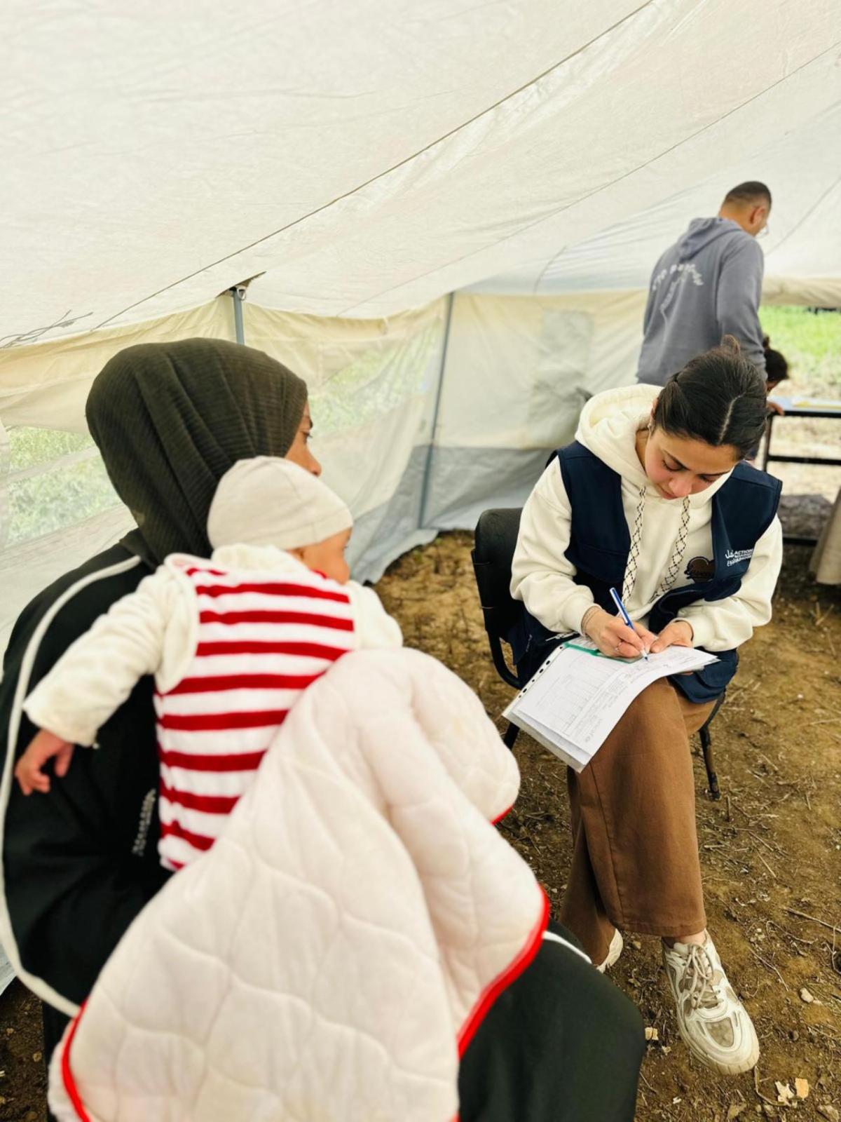 Woman holds baby while being assessed by an Action Against Hunger staff member. 
