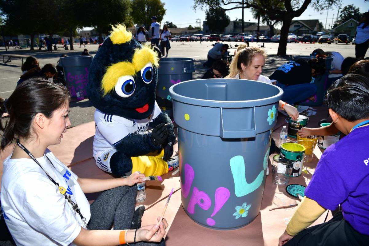 AEG volunteers join LA Galaxy's mascot Cozmo to paint trash cans.