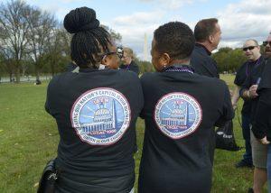 The backs of two people sitting close together, looking at each other. The Washington Monument in the distance.