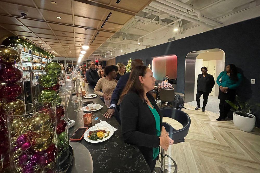 A group of people eating at a long bar, standing and turned to face the opposite side of the room.