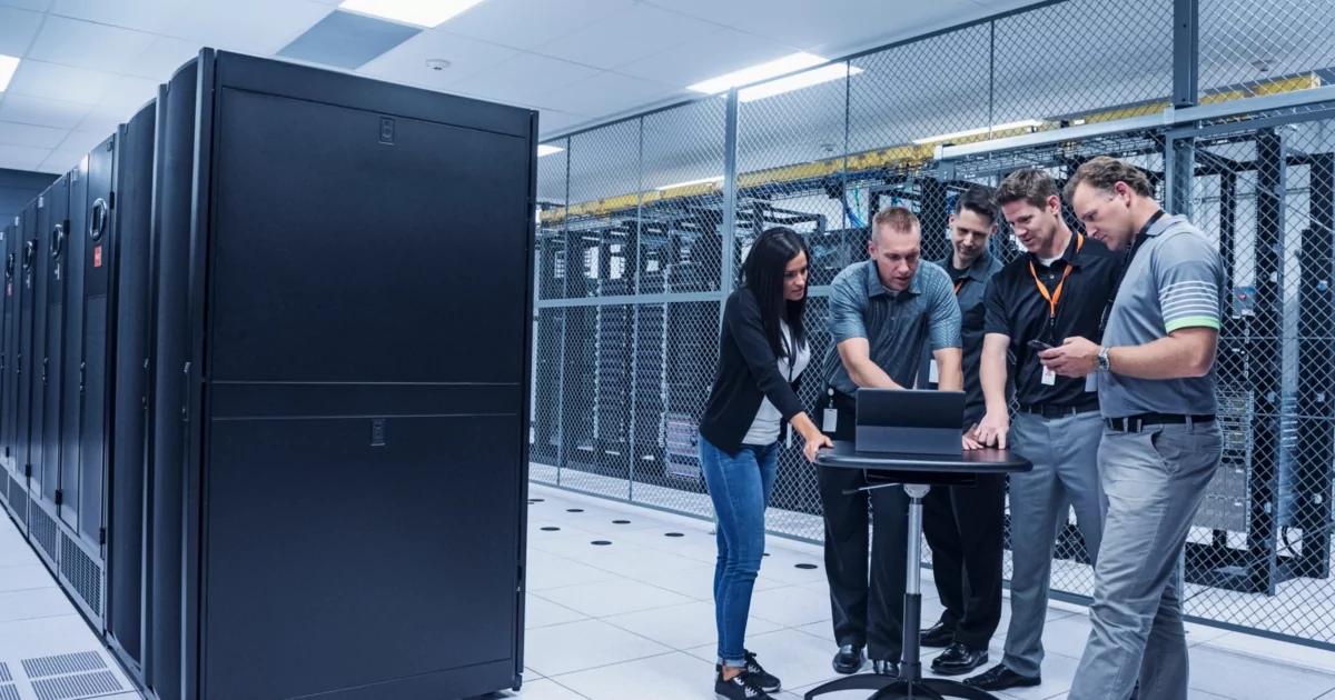 5 people looking at a laptop around servers