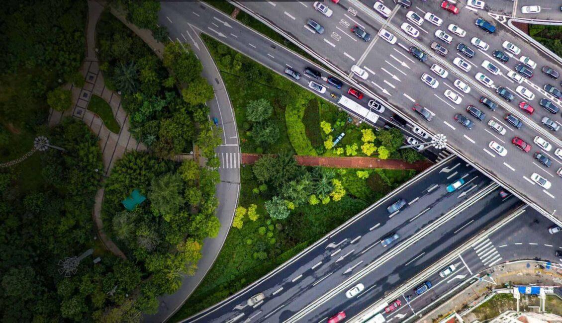 Aerial view of intersecting highways and traffic. An area of trees and grass are central and to the left side.