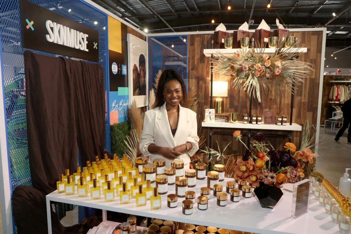 SKNMUSE Owner, Ezinne Tracey Iroanya-Adeoye posing behind a table containing her skin care products.