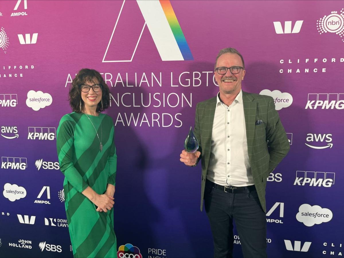 Two people stood in front of an Australian LGBTQ Inclusion Awards event back drop