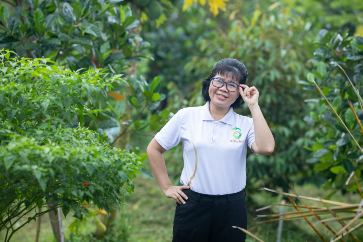 Nguyen Thi Kim Thoa standing in an orchard, touching the side of her glasses. Wearing an Abavina logo shirt