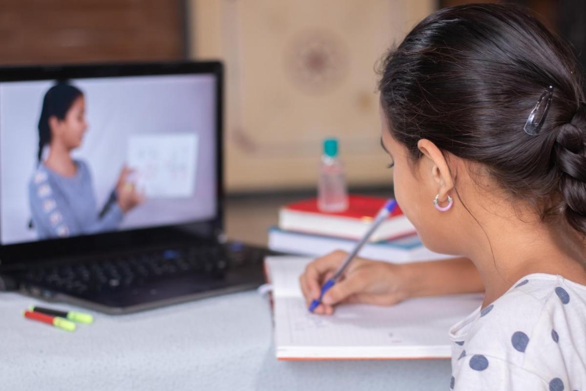 student writes in a notebook while watching a laptop screen